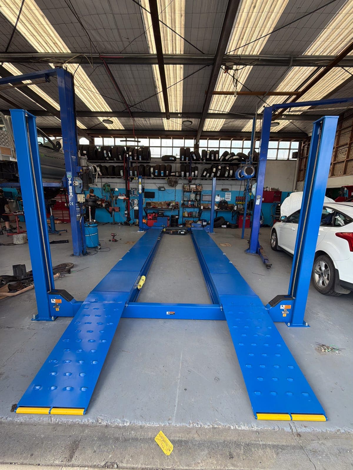Blue four-post wheel-alignment hoist installed in a working workshop